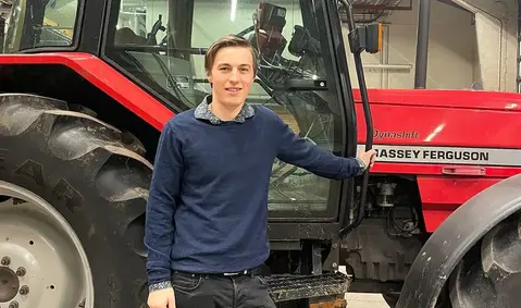 En person i mörkblå tröja står vid en röd traktor.
