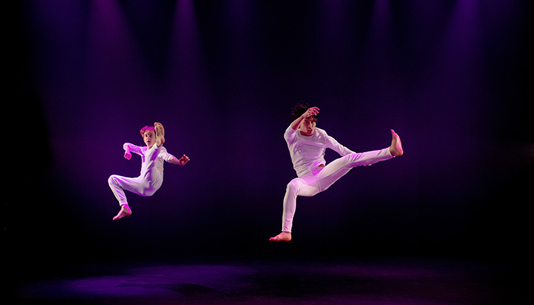 Två killar i vita kläder flyger i luften i ett danssteg.