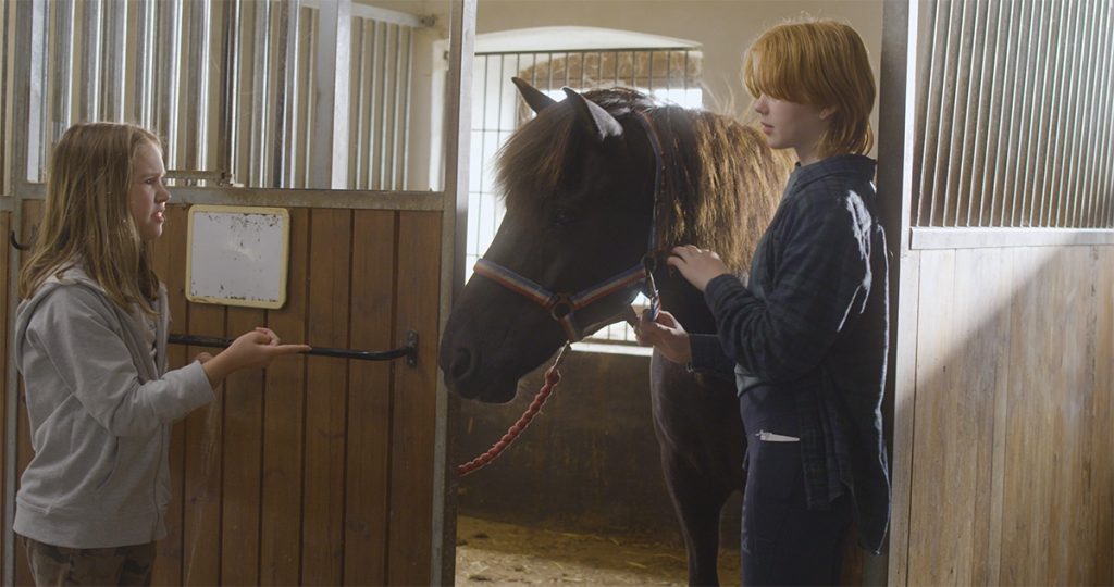 Klipp ur filmen Åsna, en scen med två tjejer och en häst i ett stall.