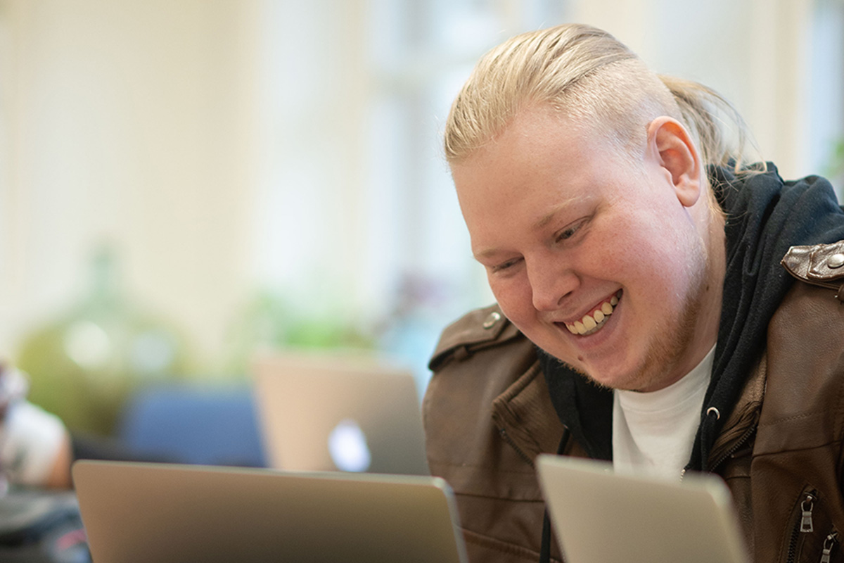 En ung person sitter vid en dator och ler stort.