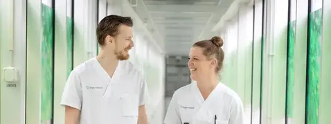 Två personer i vita vårdkläder i en korridor.