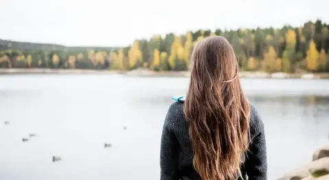 En ung person med långt hår tittar ut över en sjö.