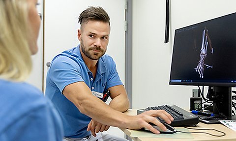 Man i blå kortärmad skjorta sitter framför en datorskärm