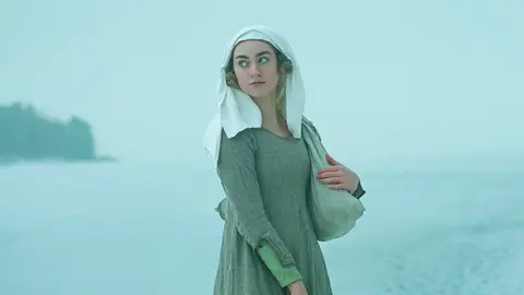 En ung kvinna i medeltidskläder står i ett vintrigt och dimmigt landskap.