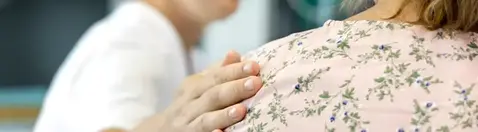 Två personer sitter bredvid varandra, den ena håller sin hand på den andras rygg.